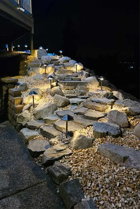 Stone walkway with landscape lighting at night, built with large rocks and decorative gravel.