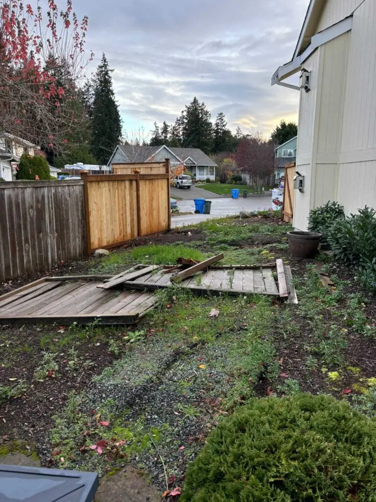 Broken wooden fence panels on the ground in a residential yard needing excavation and site clearing.