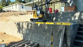 Mini excavator on a retaining wall during site preparation and leveling project.