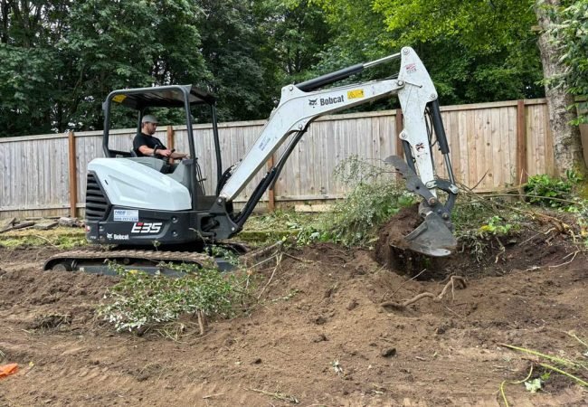 Mini excavator digging and clearing roots in a residential yard during site preparation.