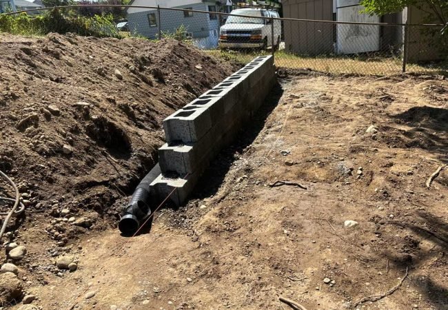 Concrete block retaining wall under construction with drainage pipe in a residential yard.