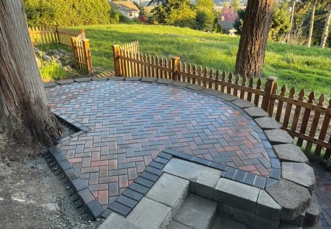 Custom paver patio with herringbone brick pattern and stone retaining wall in a residential backyard.